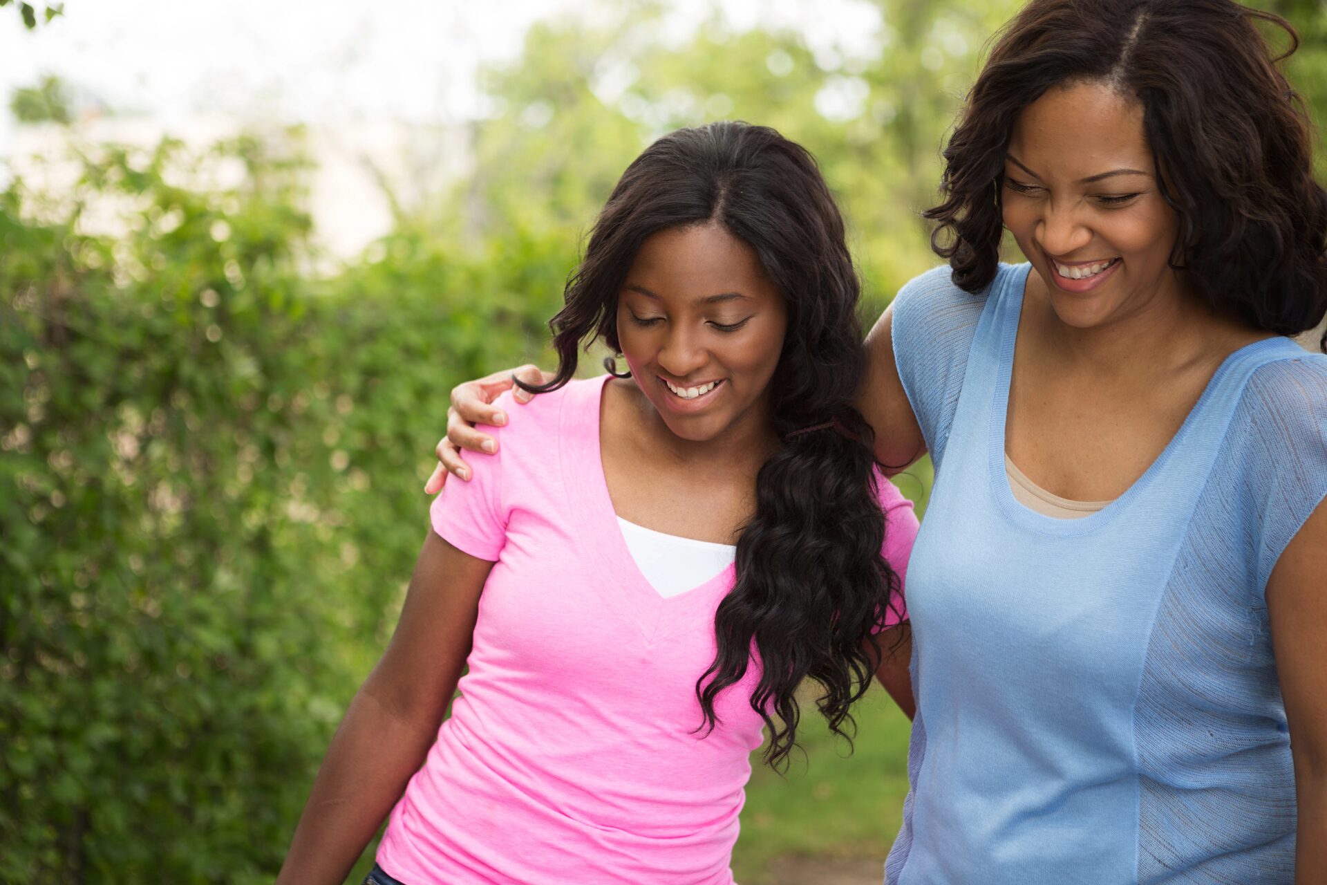 A mother and daughter walking together, arm in arm, smiling.